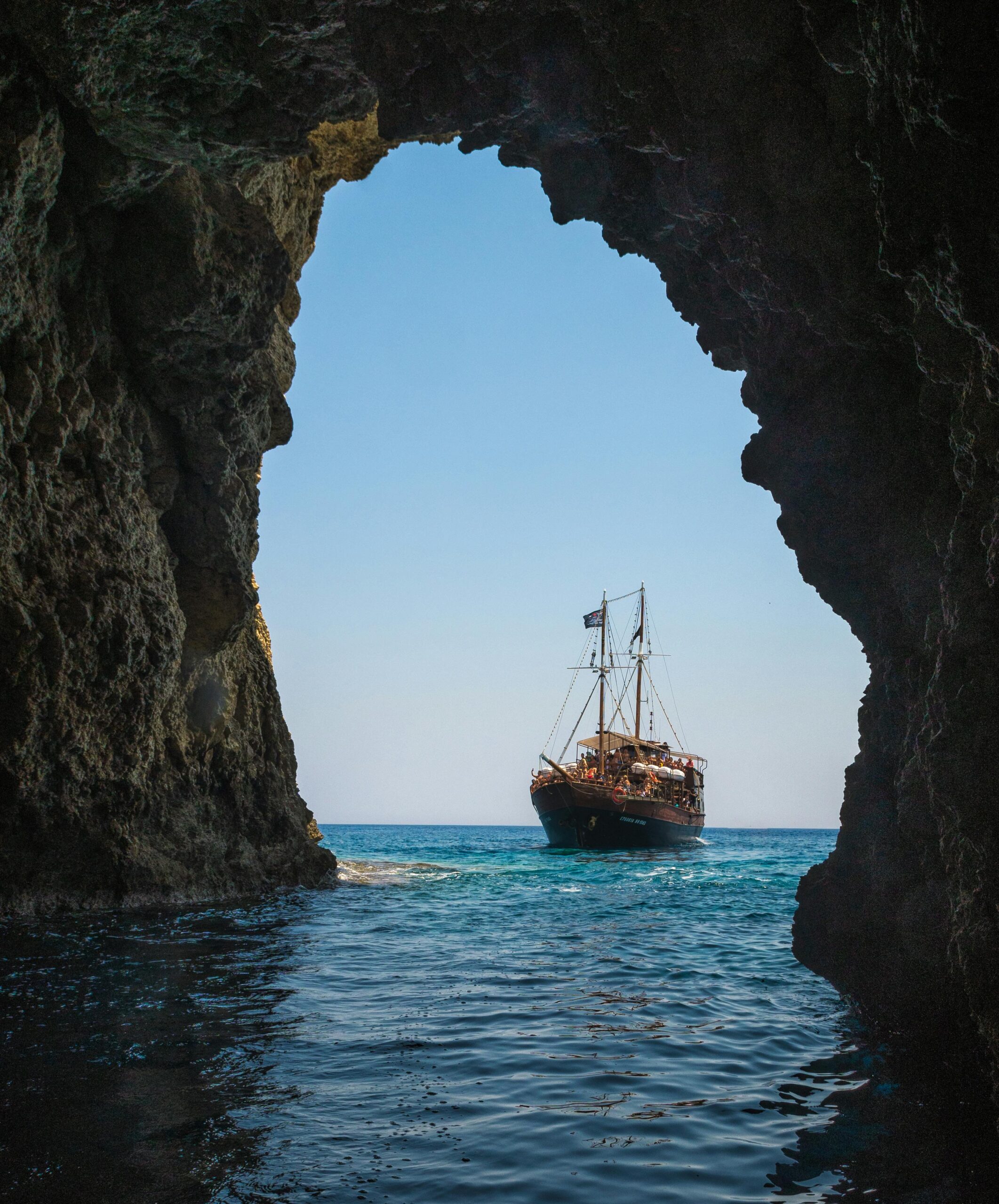 Home A stunning view of a ship sailing through a rocky sea cave in Rethymno, Greece.
